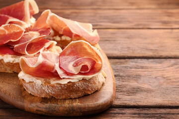 Board of tasty sandwiches with cured ham and cream cheese on wooden table, closeup. Space for text