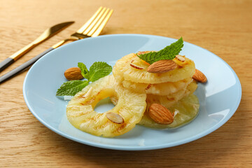 Tasty grilled pineapple slices, almonds and mint on wooden table, closeup