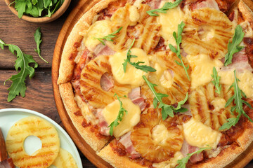 Delicious pineapple pizza and ingredients on wooden table, flat lay