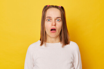 Shocked astonished teenage girl in jumper with ponytails stares bugged eyes feels anxious looks in...