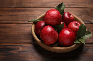 Ripe red apples and green leaves in bowl on wooden table. Space for text