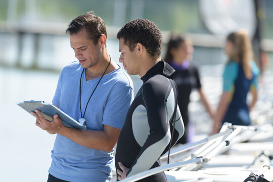 coach with stopwatch and clipboard talking to man in wetsuit
