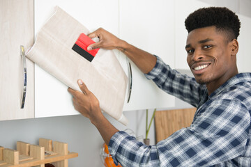 man refurbishing kitchen cupboard with adhesive veneer