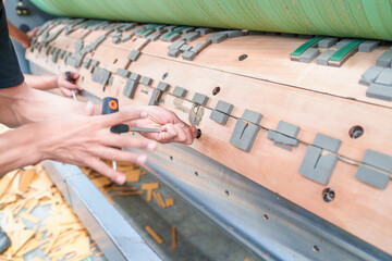 Technician using screwdriver to rotational die cutting plate for corrugated board factory machine of the corrugated board production line at packaging boxes factory,