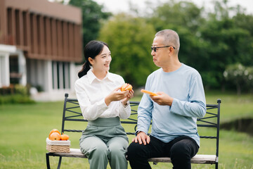 Happy adult granddaughter and senior grandfather having fun enjoying talk while relaxing sitting outdoor in park
