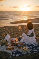 Young woman having beautiful tasty picnic with lemonade, fresh fruits and croissants on a beach at sunset.