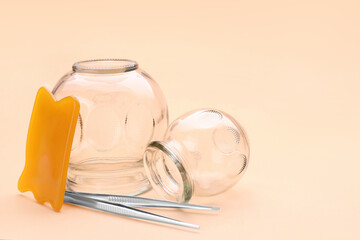 Glass cups, gua sha and tweezers on light coral background, closeup with space for text. Cupping therapy