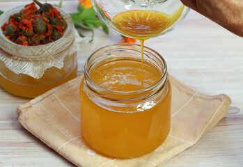 Pouring melted natural beeswax into warm herbal ointment. Woman hand holding a bowl with bee wax. Natural cosmetics from marigold flowers.