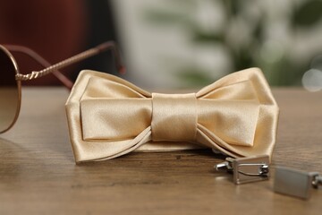 Stylish beige bow tie, sunglasses and cufflinks on wooden table, closeup
