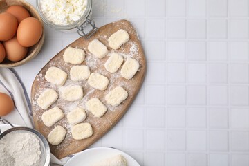 Making lazy dumplings. Board with cut dough and ingredients on white tiled table, flat lay. Space...