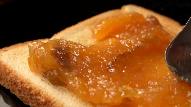 Spoon picks up cooked orange jam from pan
