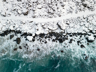 Path in the snow next to a wild shore with waves of blue ocean. Aerial view of dangerous winter pathway in Norway. - 649684293