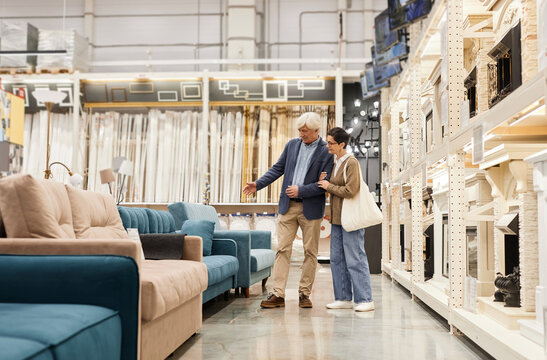 Side view full length portrait of senior couple looking at furniture in home improvement store, copy space