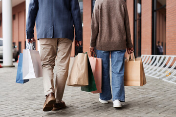 Back view of adult couple with shopping bags walking together outdoors by mall, copy space
