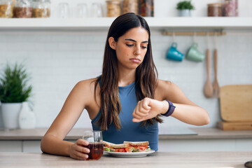 Hungry sporty woman waiting for the time to eat healthy breakfast after fasting in the kitchen at...