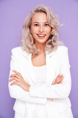 Portrait of young beautiful blond woman wearing nice trendy white suit. Fashion model posing in studio. Fashionable female isolated on violet background. Cheerful and happy