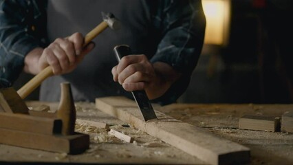 Crafting table. A woodworker works with a chisel, knocks chips out of wood, works with a tool in a woodworking shop, a wood specialist processes the material independently, at the workplace