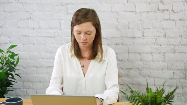 A young woman working on a laptop comuter in a white walled office with plants and a coffee cup