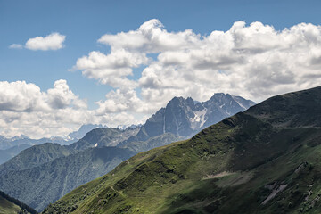 Fototapeta premium Mountain landscape with green slopes, cliffs, glaciers and white clouds in the sky