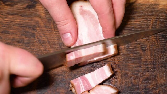 Slicing of salted pork fatback on cutting board, close-up. Ukrainian traditional food - salo	
