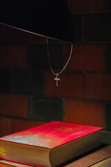 eine Kette mit einem kleinem, goldenem Kreuz über einer roten Bibel hängend