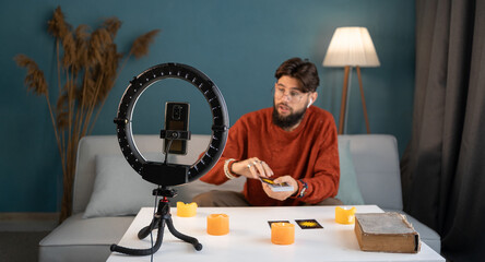 Young male fortune-teller with tarot cards recording video for blog at home.