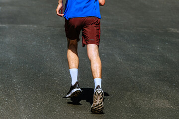Fototapeta premium rear view male runner running uphill on background dark asphalt, summer marathon race