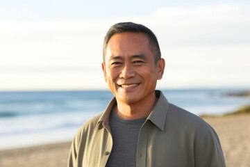 portrait of a confident Filipino man in his 50s wearing a chic cardigan against a beach background