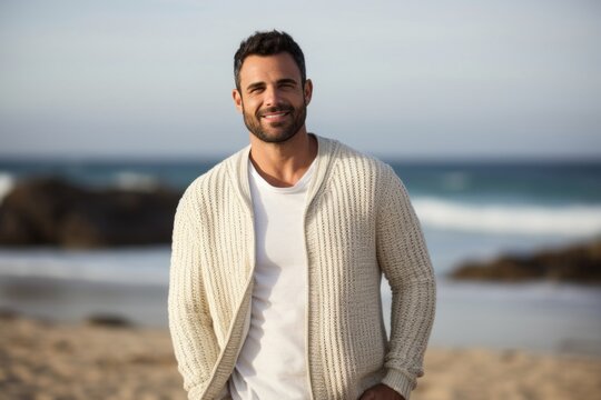 portrait of a confident Israeli man in his 30s wearing a chic cardigan against a beach background