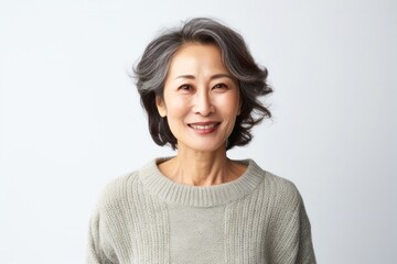 Fototapeta premium portrait of a confident Japanese woman in her 50s wearing a cozy sweater against a white background