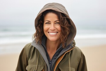 Portrait of a happy Israeli woman in her 40s wearing a warm parka against a beach background - obrazy, fototapety, plakaty