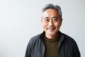 Portrait of a happy Japanese man in his 60s wearing a chic cardigan against a minimalist or empty room background