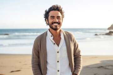 portrait of a confident Mexican man in his 20s wearing a chic cardigan against a beach background