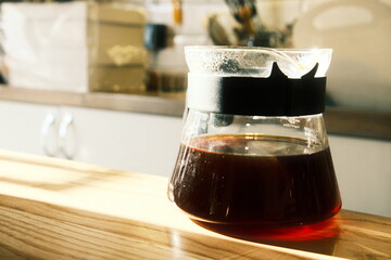 A glass decanter on a light wooden tabletop holding freshly brewed black craft coffee