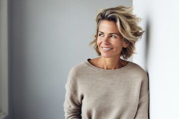 Fototapeta premium Portrait of a happy Polish woman in her 40s wearing a chic cardigan against a minimalist or empty room background