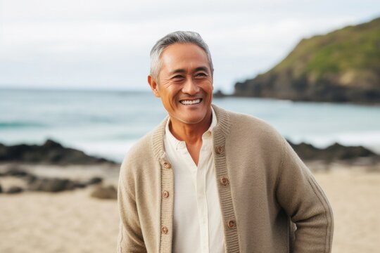 Portrait of a Filipino man in his 50s wearing a chic cardigan against a beach background
