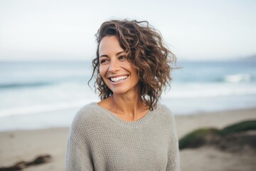 Portrait of a Israeli woman in her 40s wearing a cozy sweater against a beach background - obrazy, fototapety, plakaty