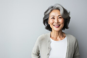 Portrait of a Japanese woman in her 50s wearing a chic cardigan against a minimalist or empty room background