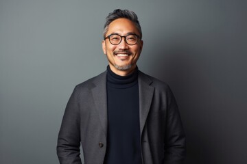 Fototapeta premium Portrait of a confident Japanese man in his 40s wearing a chic cardigan against a minimalist or empty room background