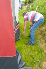 Taking down the awning, man bends and uses hook to remove tent pegs that have been holding awning in place after a holiday in caravan.