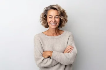 Fotobehang medium shot portrait of a happy Israeli woman in her 40s wearing a cozy sweater against a white background © Anne-Marie Albrecht