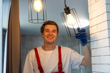 Worker installing lamp on stretch ceiling indoors.