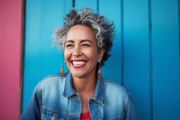medium shot portrait of a happy Mexican woman in her 60s wearing a denim jacket against an abstract background