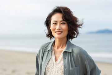 portrait of a happy Japanese woman in her 40s wearing a chic cardigan against a beach background