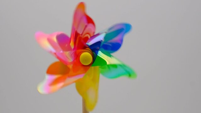 A front view of a group of regular toy pinwheel windmills with six differently psychedelic colored vanes rotating on a stick on a white screen background