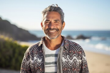 portrait of a happy Mexican man in his 50s wearing a chic cardigan against a beach background