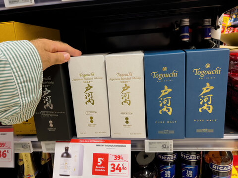 Paris, France - Sep 18, 2023: A man's hand is seen in a French Auchan supermarket, reaching for bottles of Togouchi Malt Whiskey, which are displayed at a special discounted price of 34.9 euros.