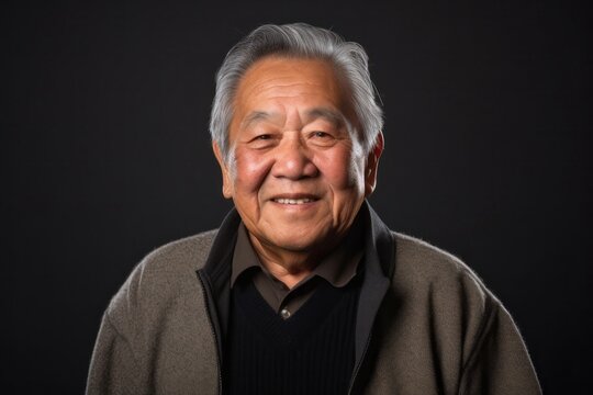 portrait of a happy Filipino man in his 70s wearing a chic cardigan against an abstract background