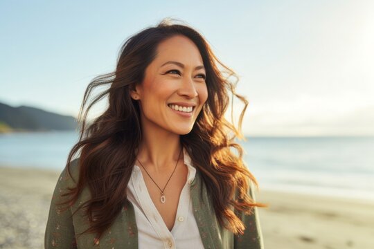 portrait of a happy Filipino woman in her 30s wearing a chic cardigan against a beach background