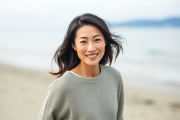 portrait of a happy Japanese woman in her 30s wearing a cozy sweater against a beach background